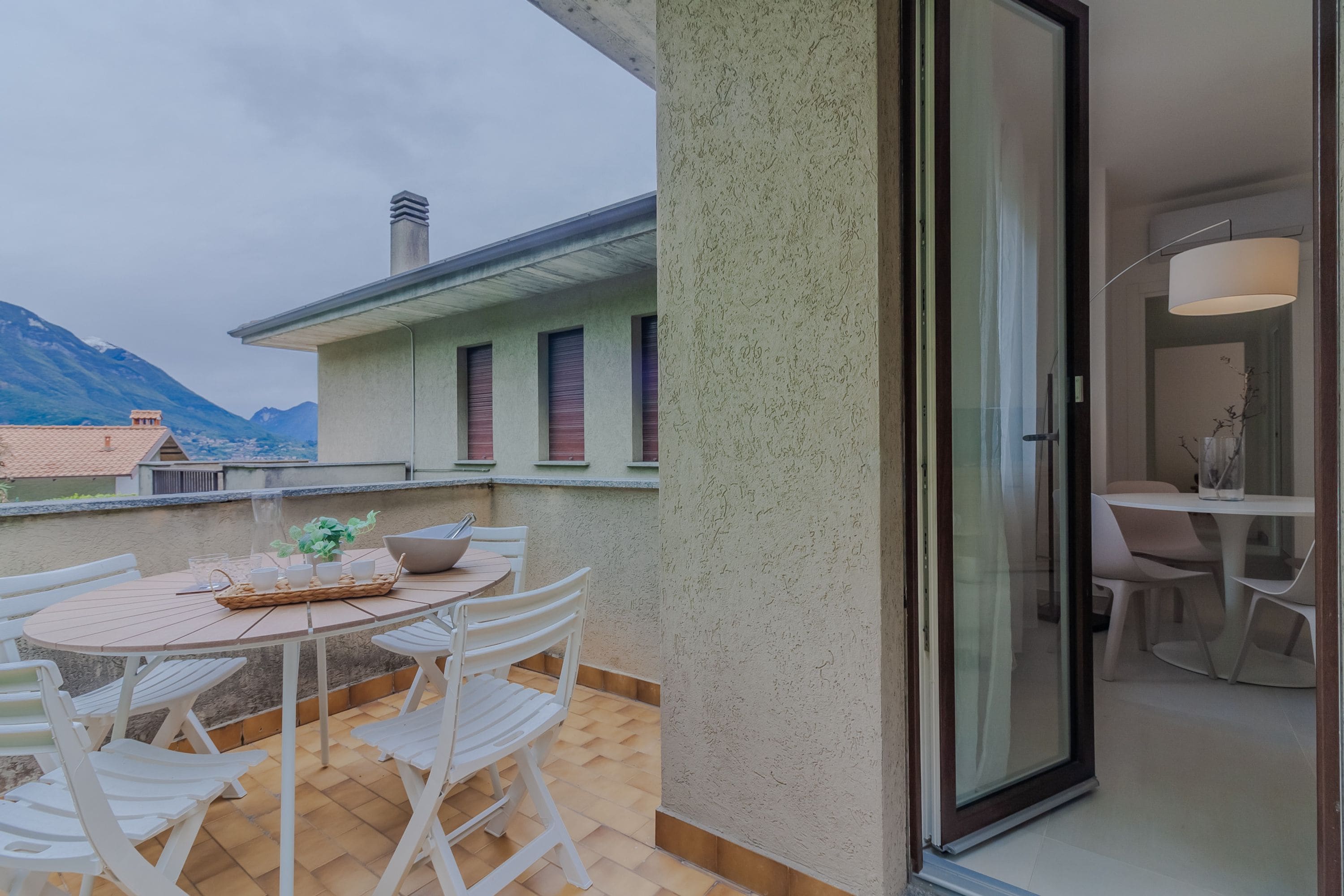 Een balkon met een tafel en stoelen, een schuifdeur en een uitzicht op bergen op de achtergrond.
