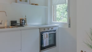 Une cuisine moderne avec des meubles blancs, un four en acier inoxydable, une machine à café et une fenêtre agrémentée de rideaux blancs.