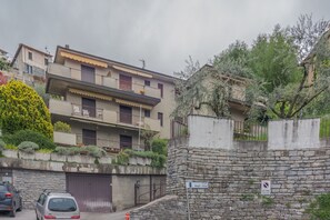 Un edificio residencial de varios pisos con balcones, un muro de piedra y un área de estacionamiento.