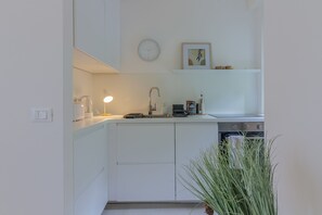 Una cocina moderna con armarios blancos, horno empotrado, cafetera y una planta en maceta.
