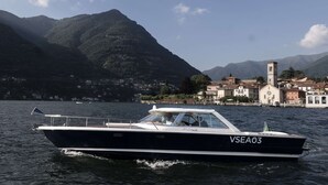 A boat named VSEA03 on a lake with a town and mountains in the background.
