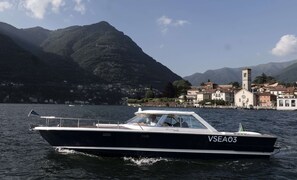 Un bote llamado VSEA03 en un lago, con un pueblo y montañas al fondo.
