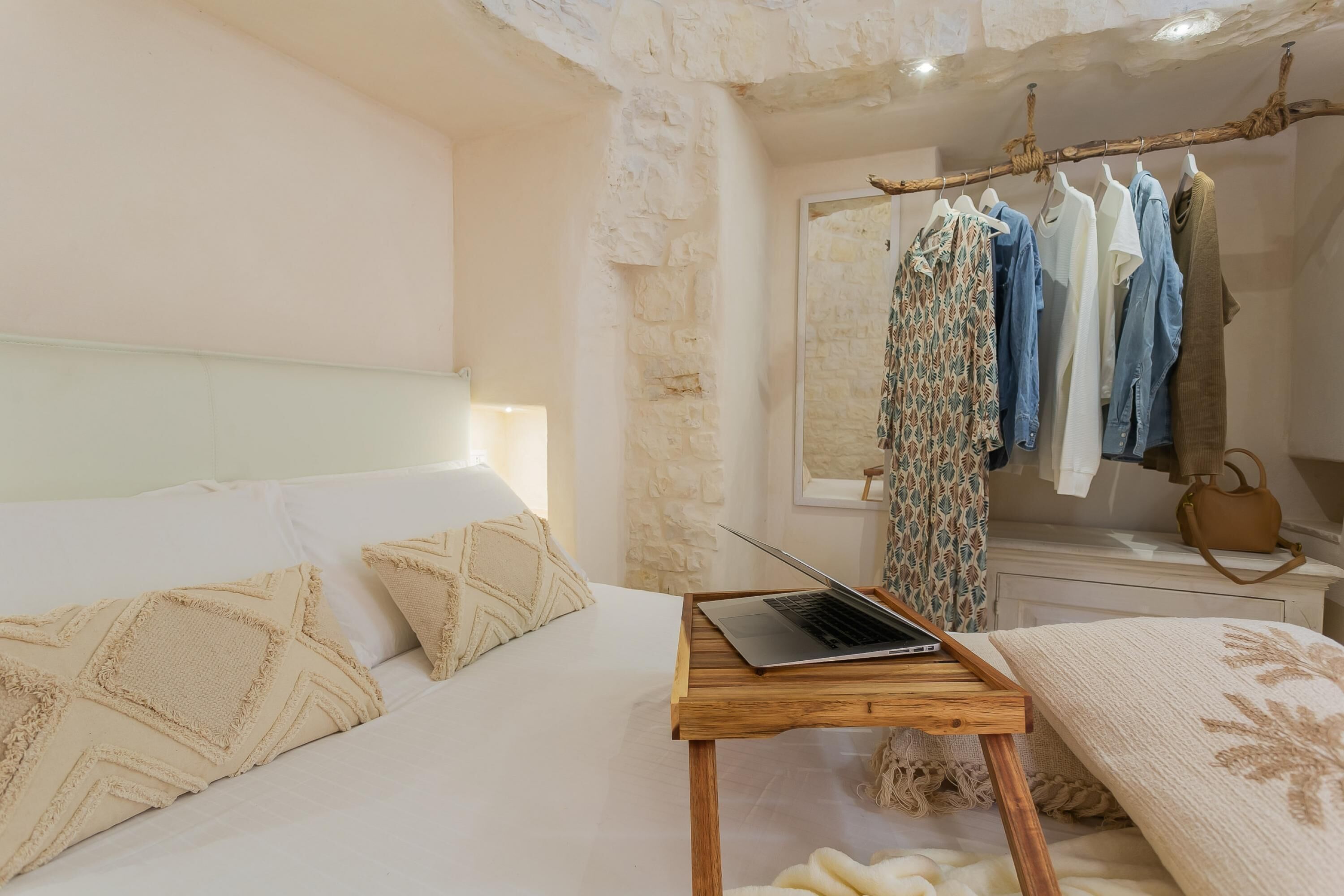 Een slaapkamer met een bed, een nachtkastje van hout met een laptop, een kledingrek en een inloopkast.