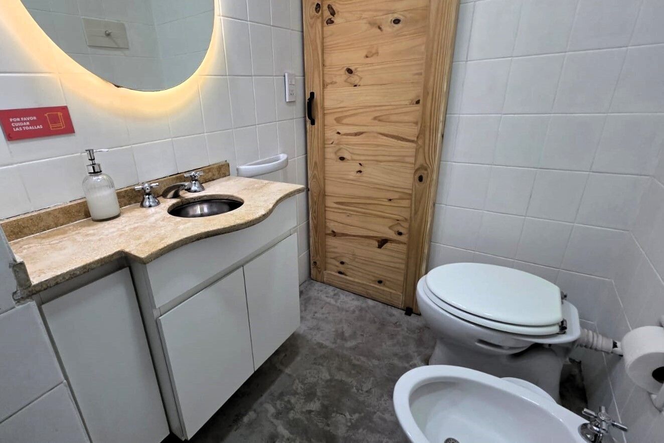 A bathroom with a wooden door, a sink with a soap dispenser, a toilet, and a bidet.