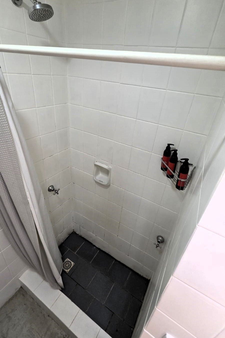 Un pequeño espacio de ducha con azulejos, un cabezal de ducha de mano, un jabonera y dos botellas de champú.