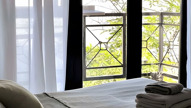 Een hotelkamer met een bed, een raam met uitzicht op groen en een stap opgevouwen handdoeken.