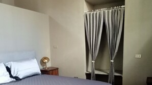 A bedroom with a bed, a nightstand, a lamp, and a window with curtains. - Palace of Alboin (Pavia)