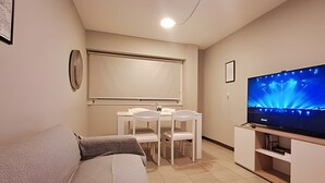 A modern living room with a grey sofa, a small dining table with chairs, a flat-screen TV on a stand, and a ceiling light. - Hornera Roca - Amplio y Cómodo, Pleno Microcentro (Rosario)