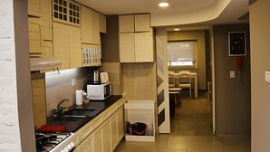 A compact kitchen with a stove, sink, and cabinets. There is a small dining area with a table and chairs. - Hornera Roca - Amplio y Cómodo, Pleno Microcentro (Rosario)