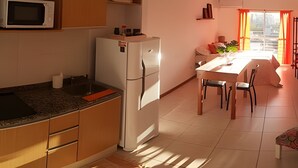 A compact kitchen with a refrigerator, microwave, and a dining area with a table and chairs. - Hornera Lagos - Modern, Spacious & Bright (Rosario)