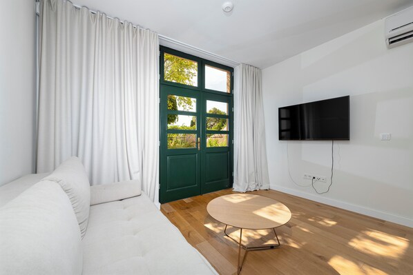 A room with a sofa, a round table, a green door, and a TV mounted on the wall.