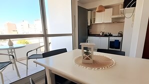 A modern kitchen with white cabinets, a dining table with chairs, and a view of the city through large windows. - Hornera San Juan - Bright Balcony Apartment (Rosario)