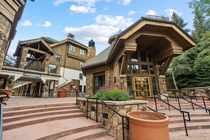 Un edificio a più piani con facciata in pietra e legno, un'ampia entrata con porte in vetro e una scala che conduce all'ingresso.