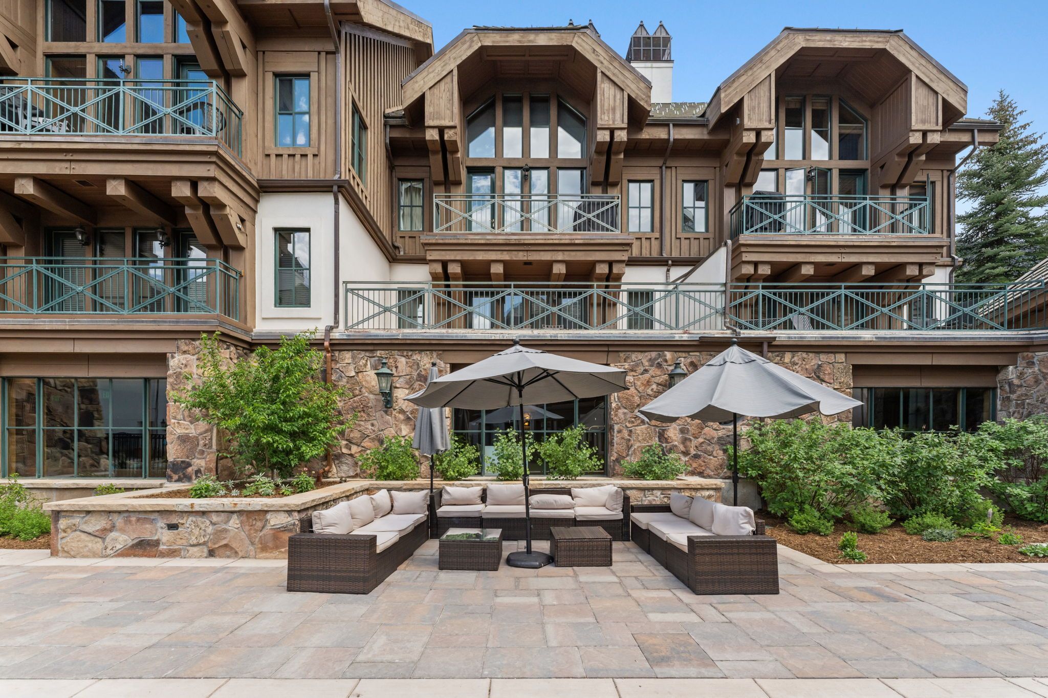 A multi-story building with a stone facade, outdoor seating area with cushions and umbrellas, and a balcony with railings.