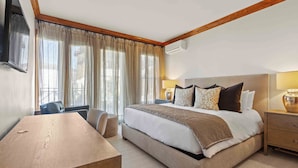 A hotel room with a large bed, a desk, a chair, and a TV mounted on the wall.