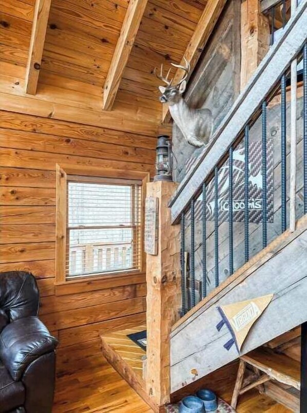 A wooden cabin interior with a fireplace, a leather chair, and a deer head decoration.
