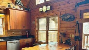 A rustic kitchen with wooden cabinets, a wooden dining table, and a clock on the wall. - Overlook the river @ Wildwood (Max Meadows)