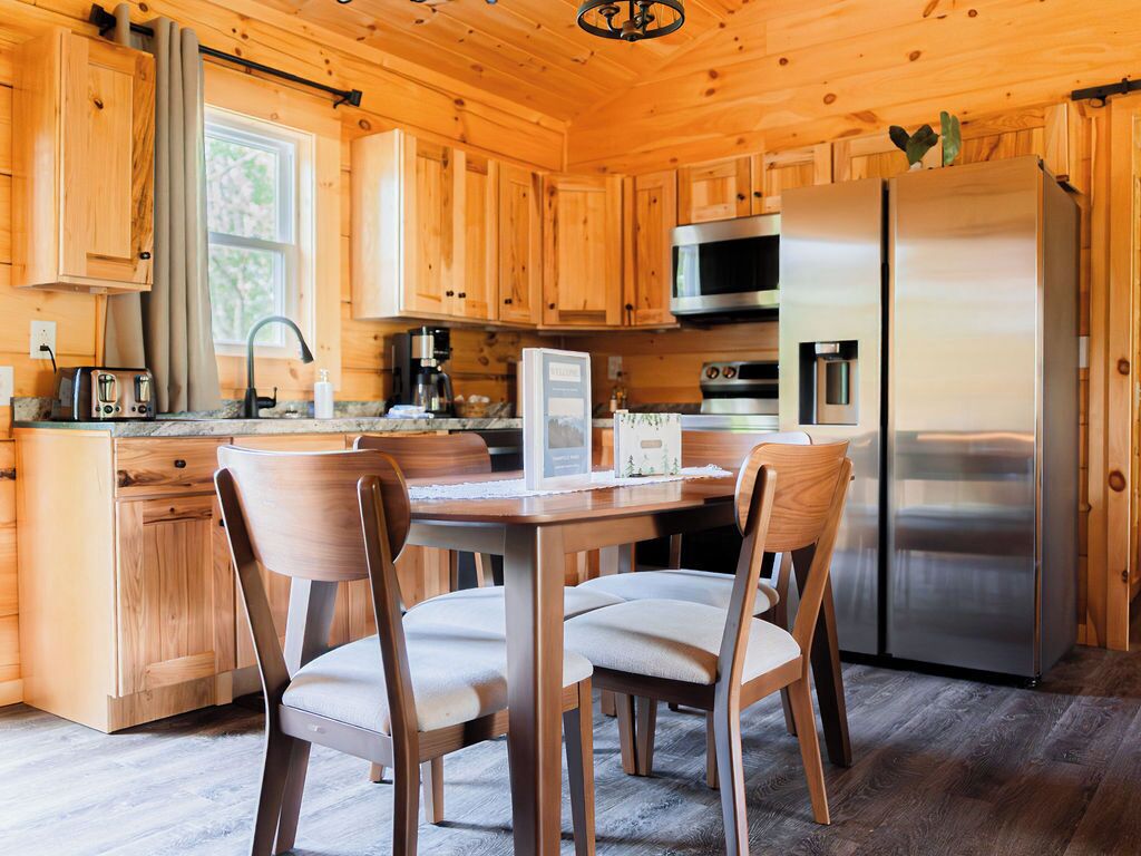 A wooden cabin kitchen with a dining table, chairs, a refrigerator, a microwave, and a coffee maker.