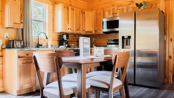 A wooden cabin kitchen with a dining table, chairs, a refrigerator, a microwave, and a coffee maker.
