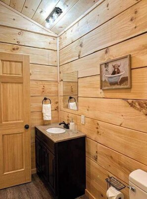 Un baño con paneles de madera, un lavabo, un espejo y un inodoro.
