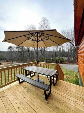 Una terraza de madera con mesa de picnic y sombrilla.