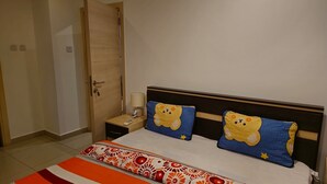 Ein Schlafzimmer mit einem Bett, zwei Kissen, einem Nachttisch, einer Lampe und einer Tür.