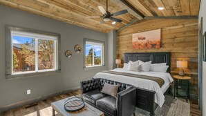 Une chambre avec un grand lit, un canapé en cuir, un ventilateur de plafond et un tableau au mur.