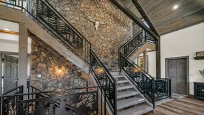 Un escalier avec un mur en pierre et des rampes en métal, menant au deuxième étage.