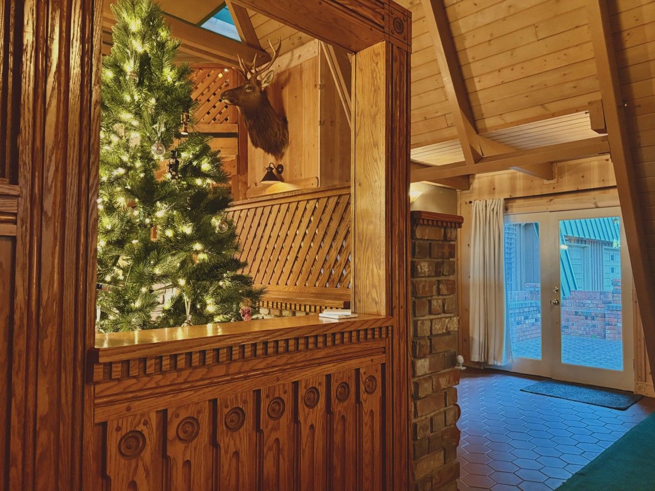Een houten interieur met een kerstboom, een decoratie van een hertenkop en een stenen muur.