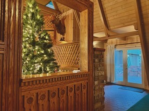 Un intérieur en bois, avec un sapin de Noël, une décoration représentant une tête de cerf et un mur en pierre.