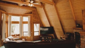 Ein gemütliches Dachzimmer mit Holzbalkendecke, einem Fernseher, einem Kamin und einem Ledersofa.