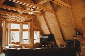 Une pièce mansardée chaleureuse avec un plafond en bois, une télévision, une cheminée et un canapé en cuir.