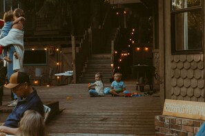 Une terrasse en bois à l’extérieur, où des enfants jouent, une pancarte indiquant « TREEHOUSE PENTHAUS », et un mur de briques.