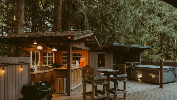 Una terrazza in legno rustico con angolo bar, posti a sedere all'aperto e una griglia.