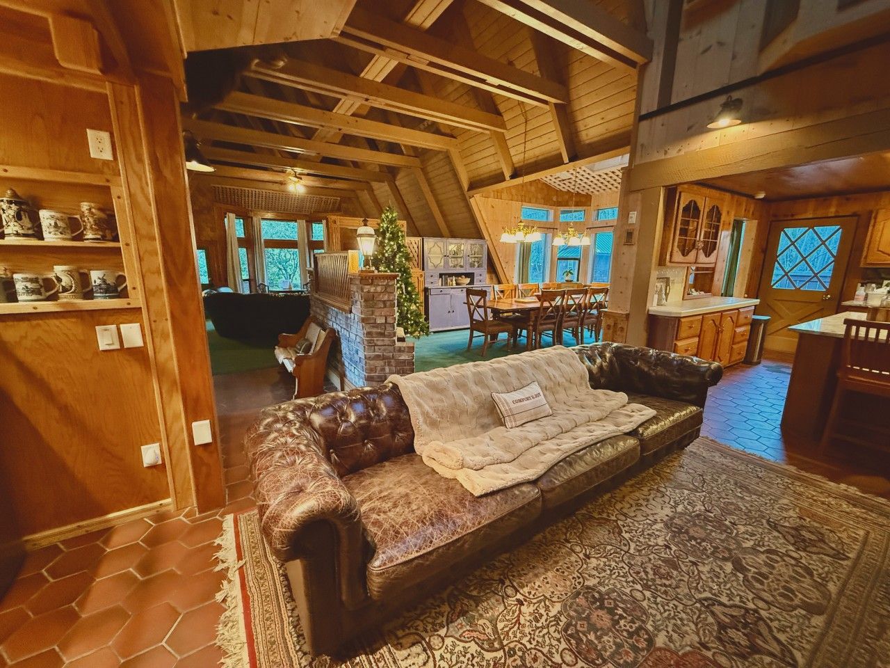 Un intérieur chaleureux avec un canapé en cuir, un tapis à motifs, des poutres en bois et un coin repas.