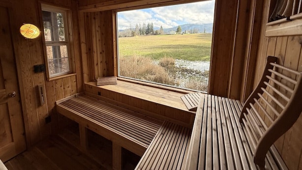A wooden cabin interior with a bench and a window overlooking a grassy field.