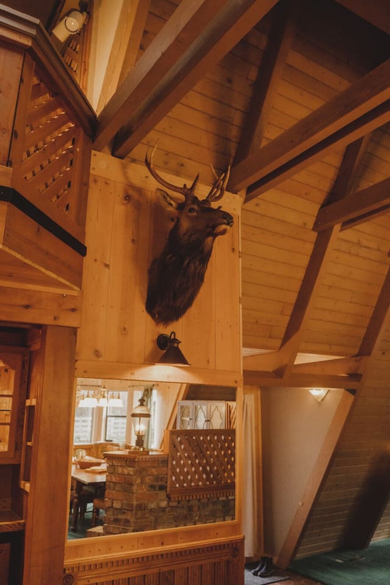 Interior de madera con un venado disecado en la pared y vigas de madera, junto a una chimenea de piedra.