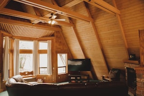 Un acogedor dormitorio en el ático con techo de madera, televisor, chimenea y sofá de cuero.