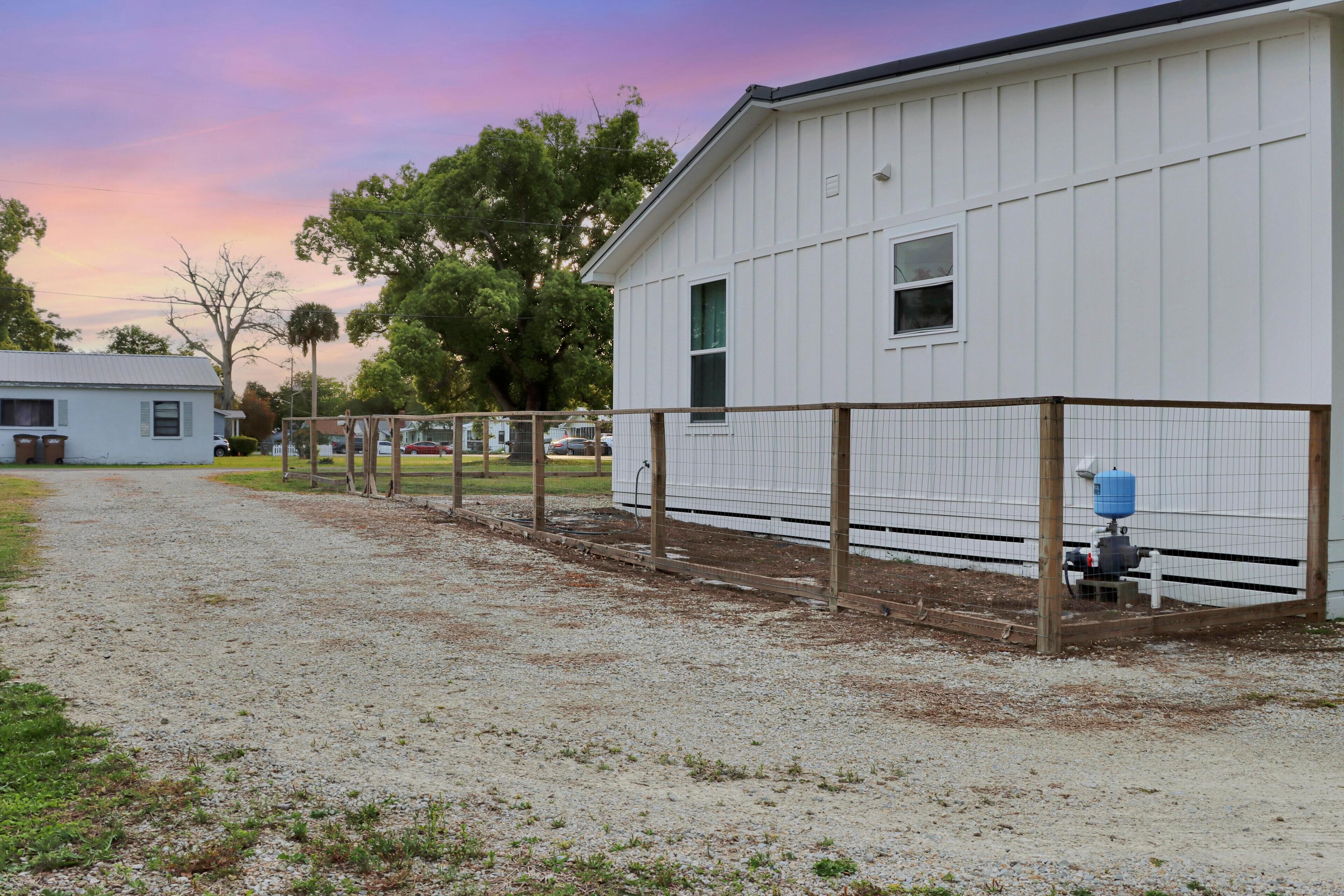 A white building with a gravel driveway and a fenced area.