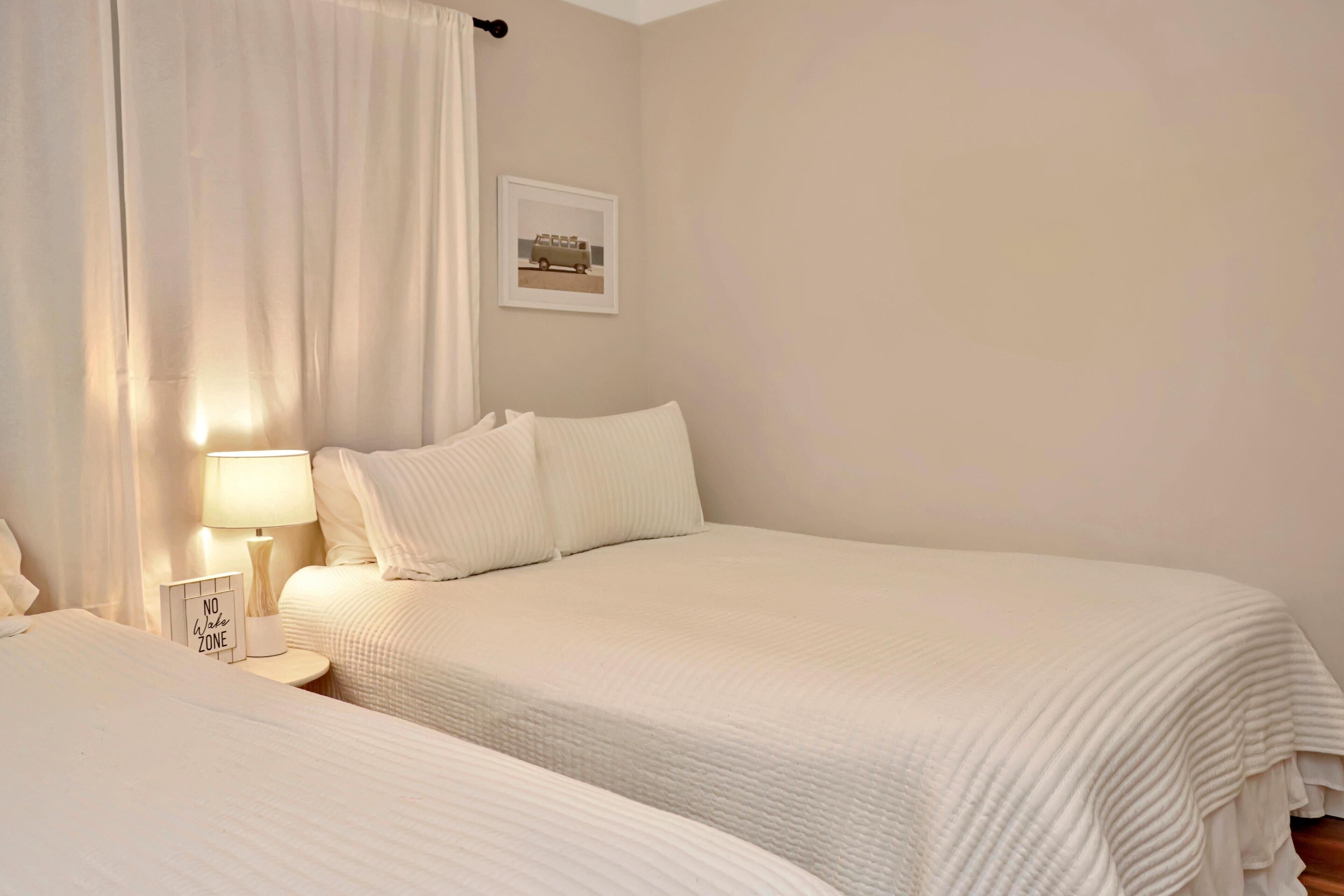 A bedroom with two beds, a bedside table with a lamp, and a framed picture on the wall.