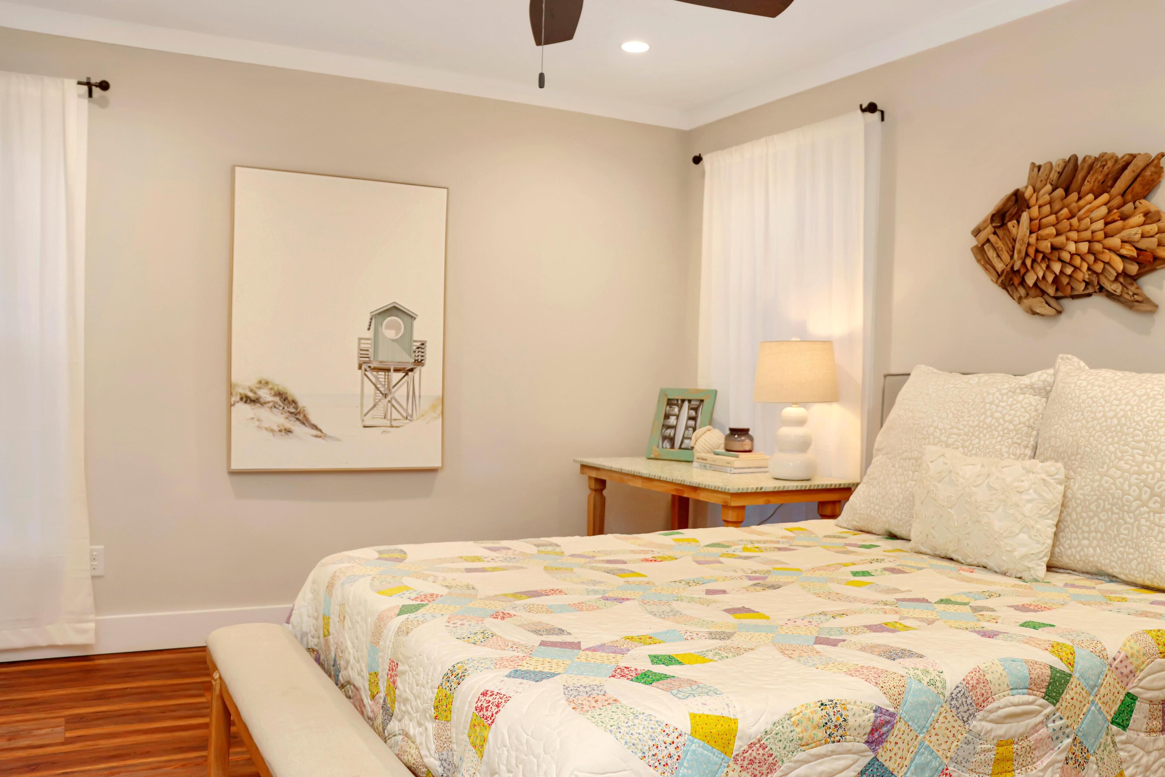 A bedroom with a large bed, a bedside table with a lamp, a framed picture, and a wall-mounted decorative piece.