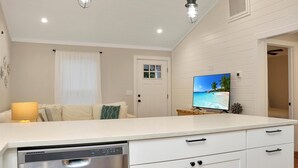 Una cucina moderna con lavastoviglie, mobili bianchi e una TV a schermo piatto montata a parete.