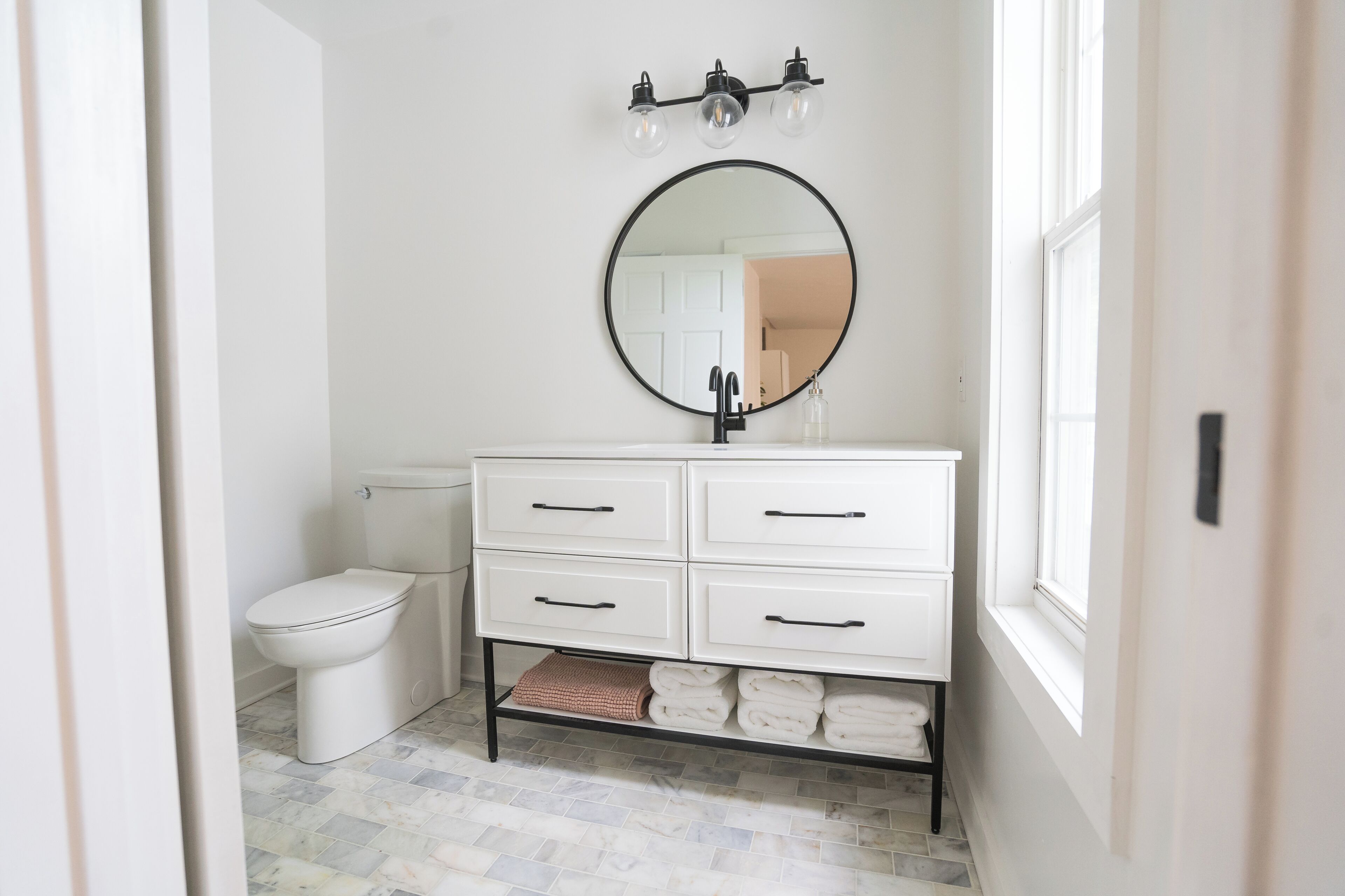 A bathroom with a white vanity, a round mirror, and a toilet.
