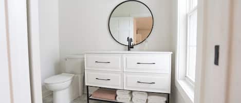 A bathroom with a white vanity, a round mirror, and a toilet.