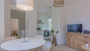 Une cuisine moderne avec des meubles blancs, un four encastré et un téléviseur posé sur un meuble en bois.