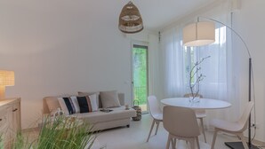 Un salon moderne comprenant un canapé, une table à manger avec des chaises, une lampe sur pied et une grande fenêtre ornée de rideaux légers.