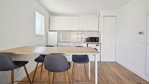 A modern kitchen with white cabinets, a wooden countertop, and a dining area with two bar stools. - Appartement Ensoleillé Avec Terrasse à Cannes (Cannes)