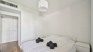 A minimalist bedroom with a bed, white walls, a white door, and a white nightstand. - Appartement Ensoleillé Avec Terrasse à Cannes (Cannes)