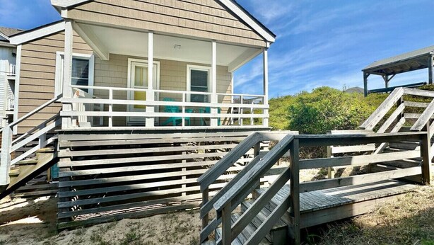 Une maison de plage dotée d’un porche couvert, d’une terrasse en bois et d’un escalier menant à l’entrée.