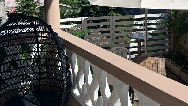 A balcony with a white umbrella, a wicker chair, and a view of the ocean. - Adorable 1Bed Cottage Walk to the Beach (St. Ann's Bay)